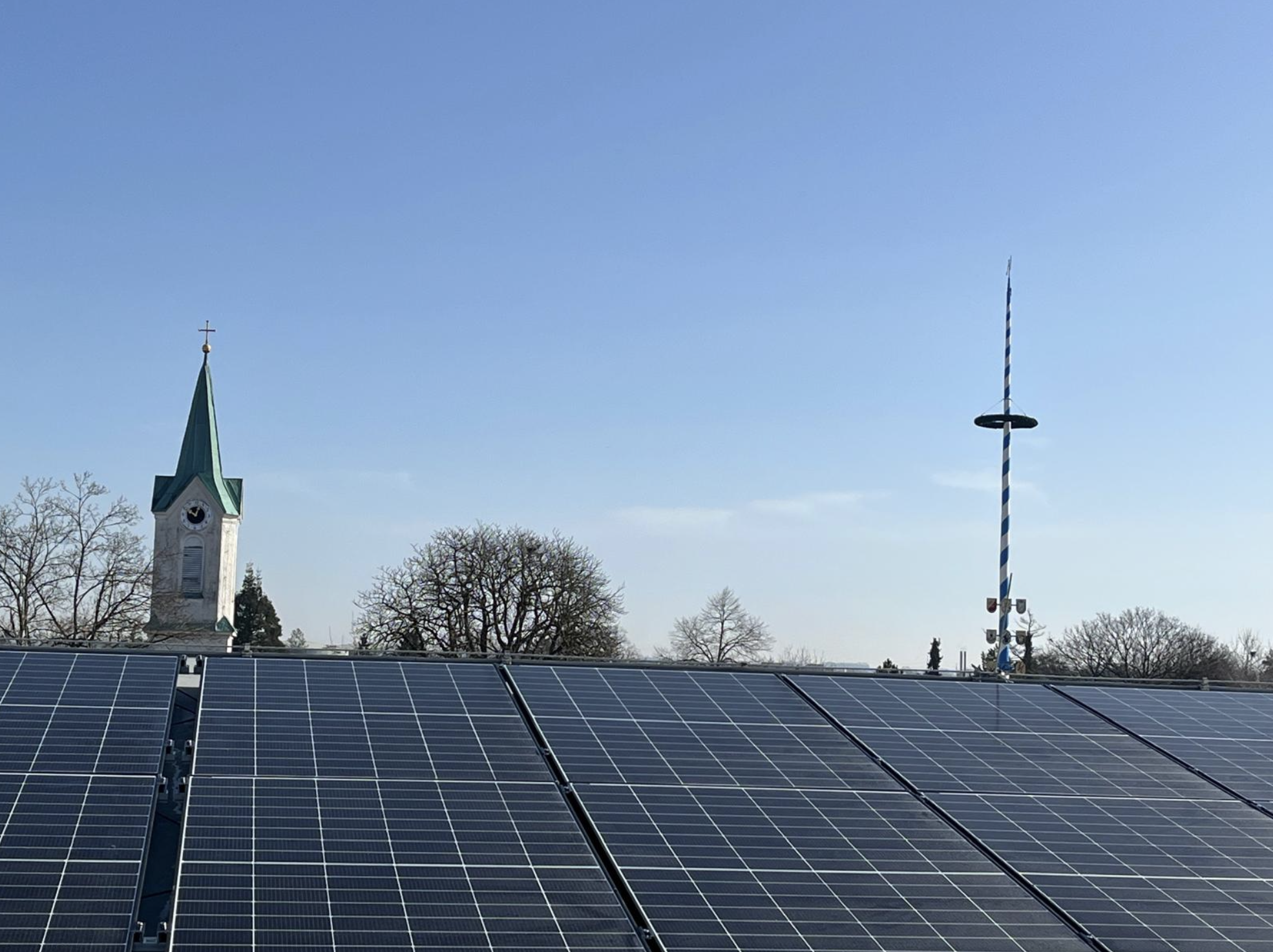 Bayerische Kirche und Maibaum hinter einer modernen Photovoltaikanlage – Tradition trifft Moderne